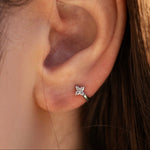 Rhodium-plated sterling silver flower huggie earring with clear cubic zirconia stones worn on the ear.