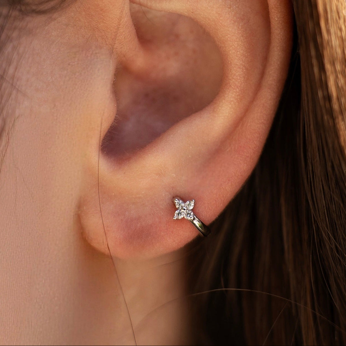 Rhodium-plated sterling silver flower huggie earring with clear cubic zirconia stones worn on the ear.