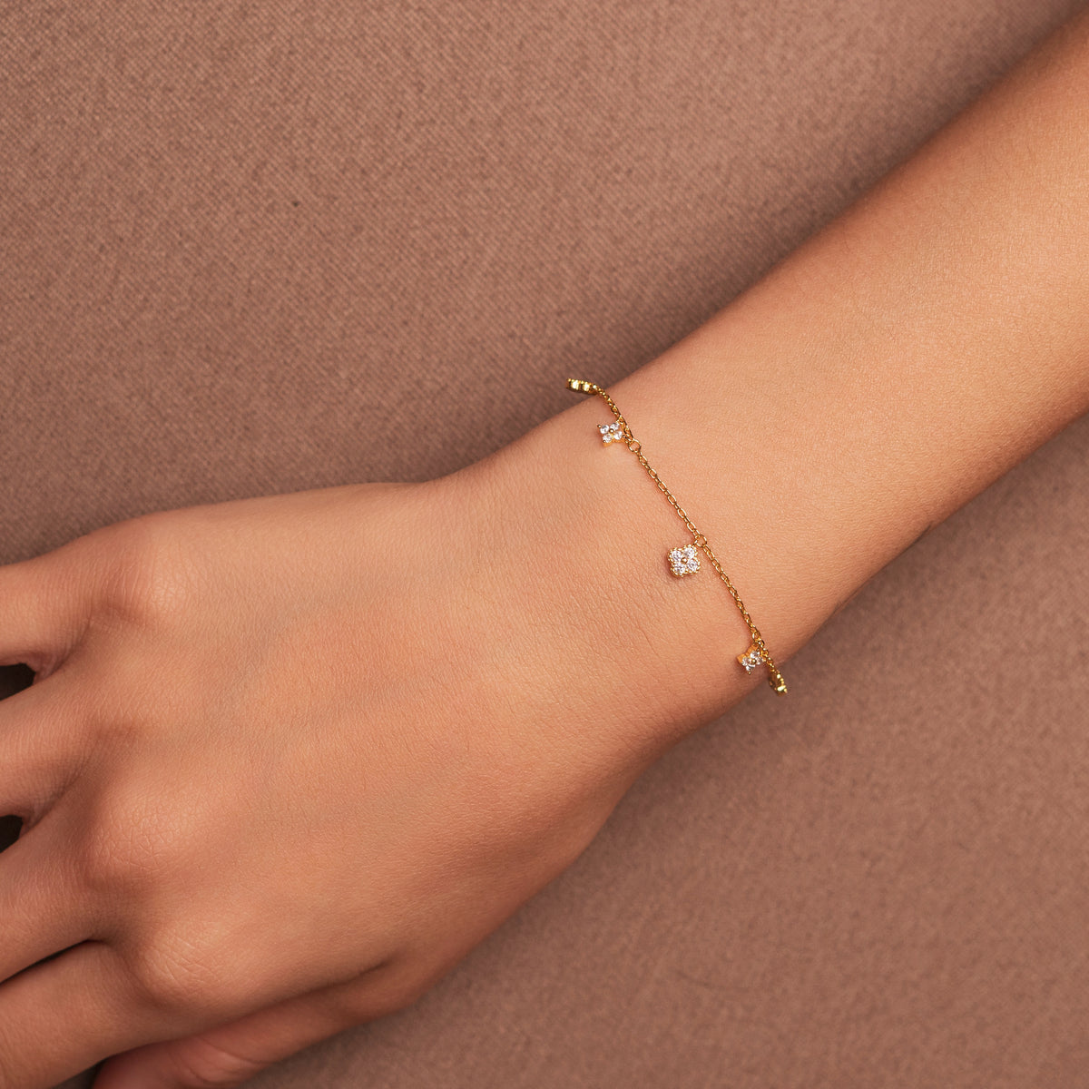 Bracelet en argent 925 plaqué or avec petits motifs fleur sertis d’oxydes de zirconium, porté au poignet