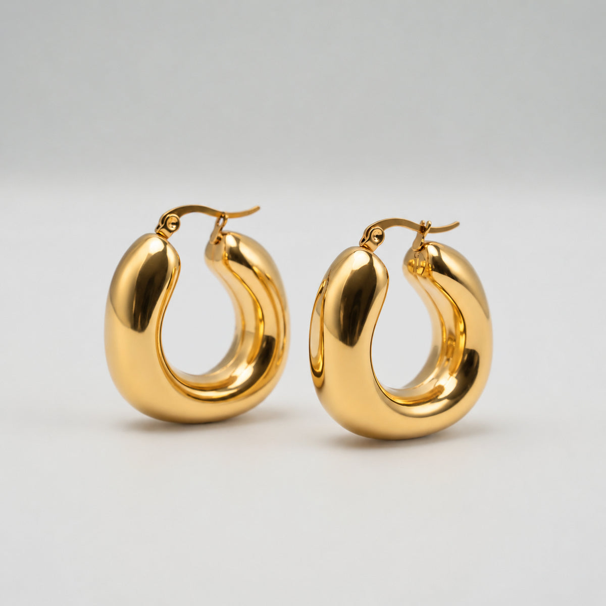 Boucles d’oreilles créoles épaisses en acier inoxydable plaqué or, à forme organique et finition lisse, sur fond clair