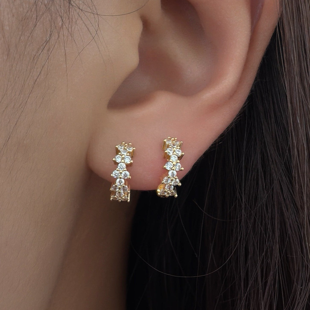 Gold-plated huggie earrings with clustered clear cubic zirconia stones worn on the ear