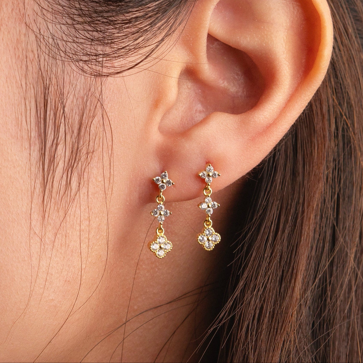 Gold-plated stainless steel drop earrings with clear cubic zirconia floral clusters worn on the ear