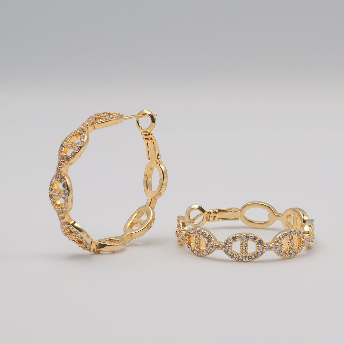 Gold-plated stainless steel hoop earrings with oval link details and clear cubic zirconia stones on a light background