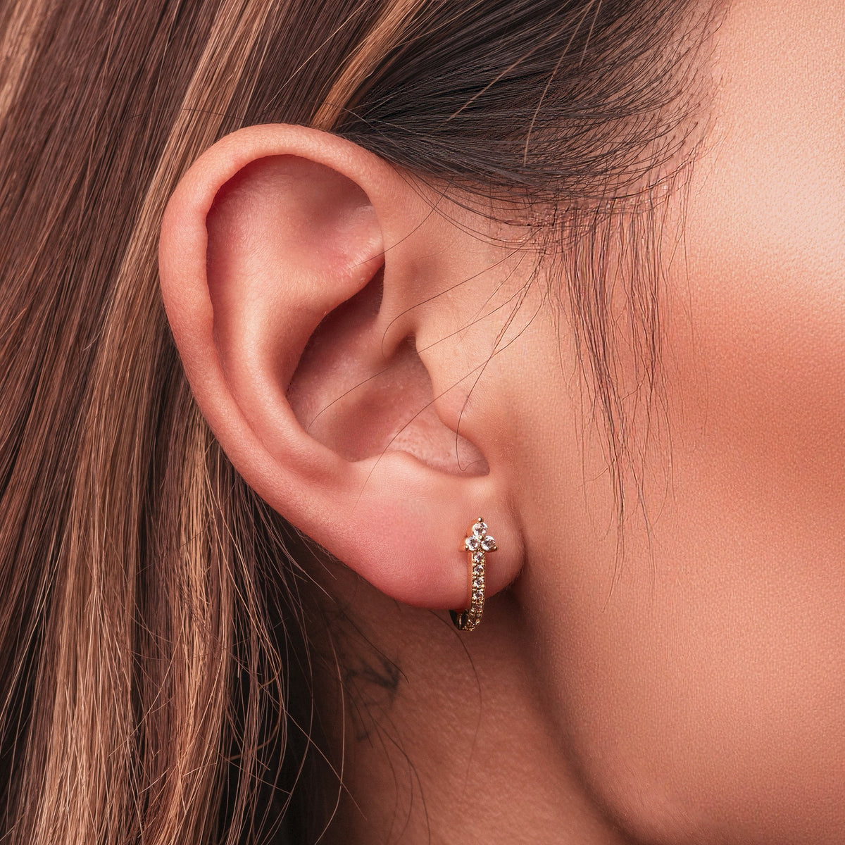 Gold-plated stainless steel rectangular huggie earrings with clear cubic zirconia stones worn on ear