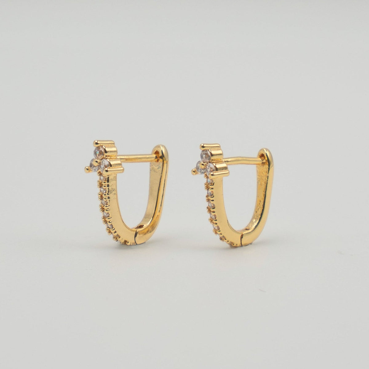 Gold-plated stainless steel rectangular huggie earrings with clear cubic zirconia stones on a light background