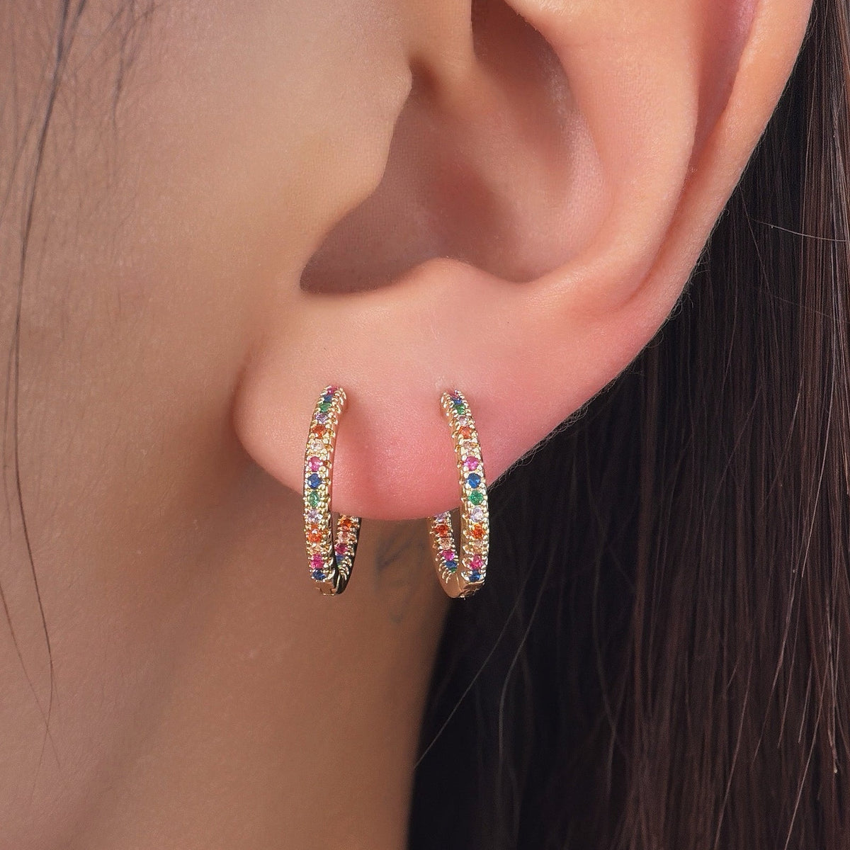 Gold-plated stainless steel hoop earrings with multicolor cubic zirconia stones worn on the ear