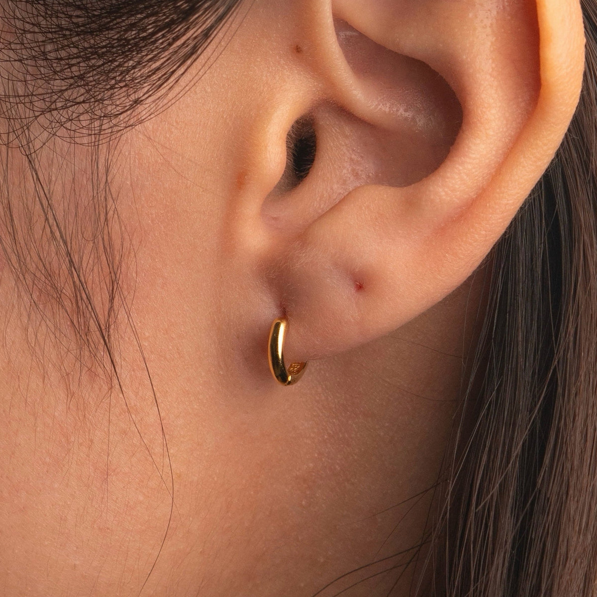 Gold-plated sterling silver classic huggie hoop earrings with a smooth polished finish worn on ear
