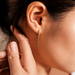 Gold-plated sterling silver huggie earring with pavé cubic zirconia and a dangling row of round cubic zirconia stones worn on the ear