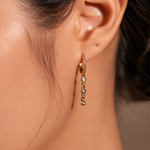 Gold-plated sterling silver huggie earring with pavé cubic zirconia and a dangling row of round cubic zirconia stones worn on the ear