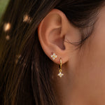 Gold-plated sterling silver hoop earrings with clear cubic zirconia star-shaped drops worn on the ear