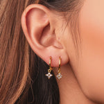 Gold-plated sterling silver hoop earrings with clear cubic zirconia star-shaped drops worn on the ear