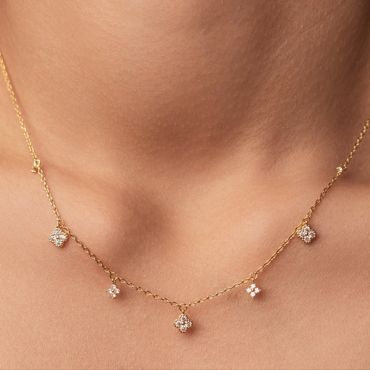 Gold-plated sterling silver necklace with five small clear cubic zirconia flower charms worn around the neck