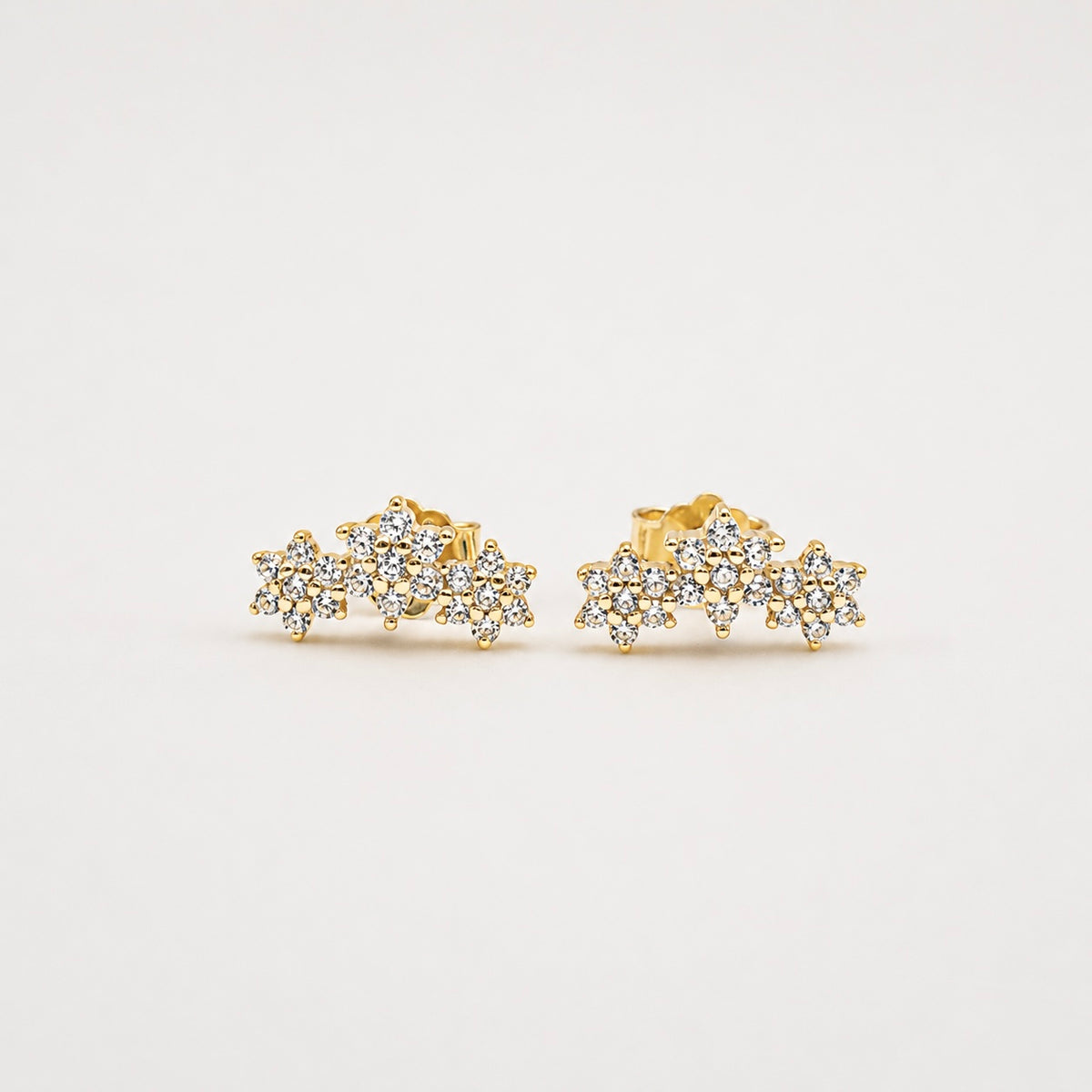Gold-plated sterling silver stud earrings with clustered floral cubic zirconia details on a light background