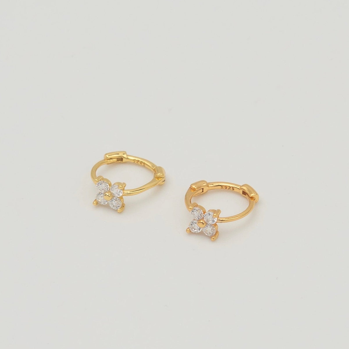 Gold-plated sterling silver huggie earrings with four-petal cubic zirconia flower details on a light background