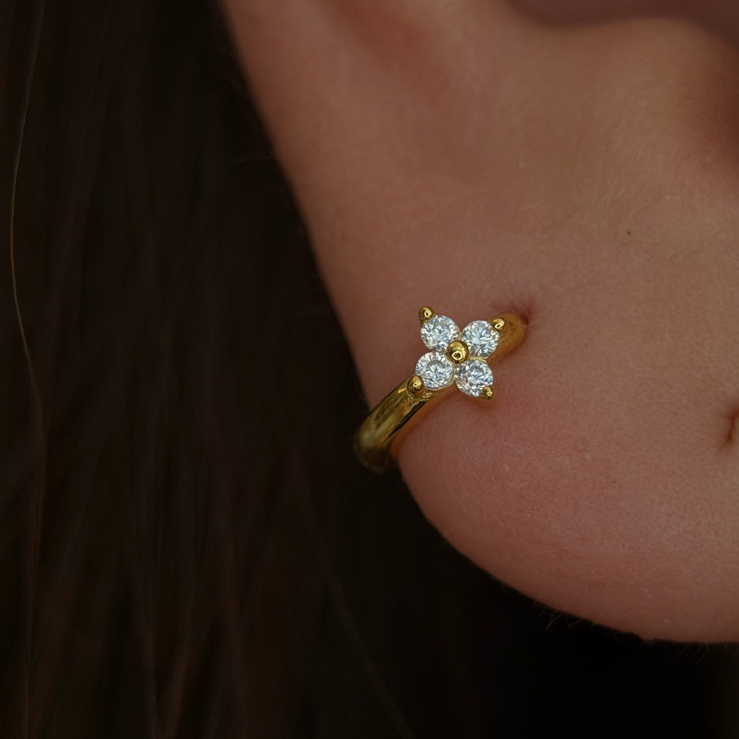 Gold-plated sterling silver flower huggie earring with clear cubic zirconia stones worn on the ear.