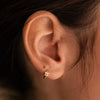 Gold-plated sterling silver huggie earring with a clear cubic zirconia flower detail worn on the ear
