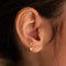 Gold-plated sterling silver huggie earring with a clear cubic zirconia flower detail worn on the ear