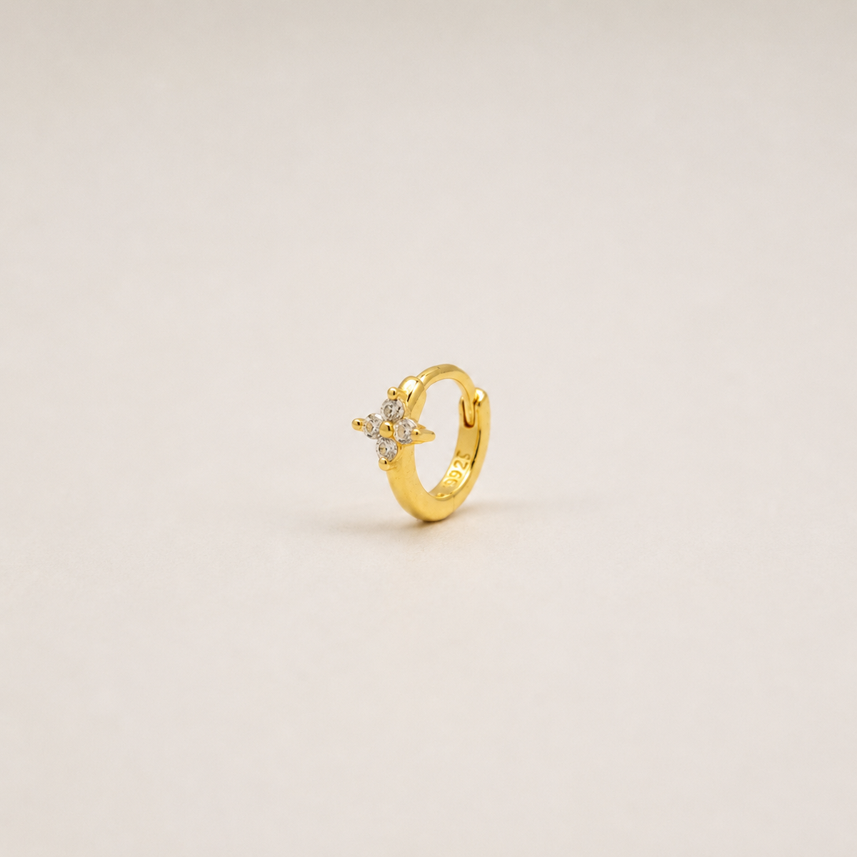 Gold-plated sterling silver flower huggie earring with clear cubic zirconia stones worn on the ear.