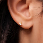 Gold-plated sterling silver flower huggie earring with clear cubic zirconia stones worn on the ear.