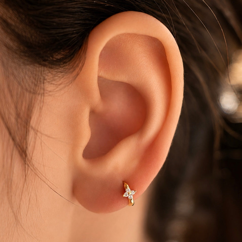Gold-plated sterling silver flower huggie earring with clear cubic zirconia stones worn on the ear.
