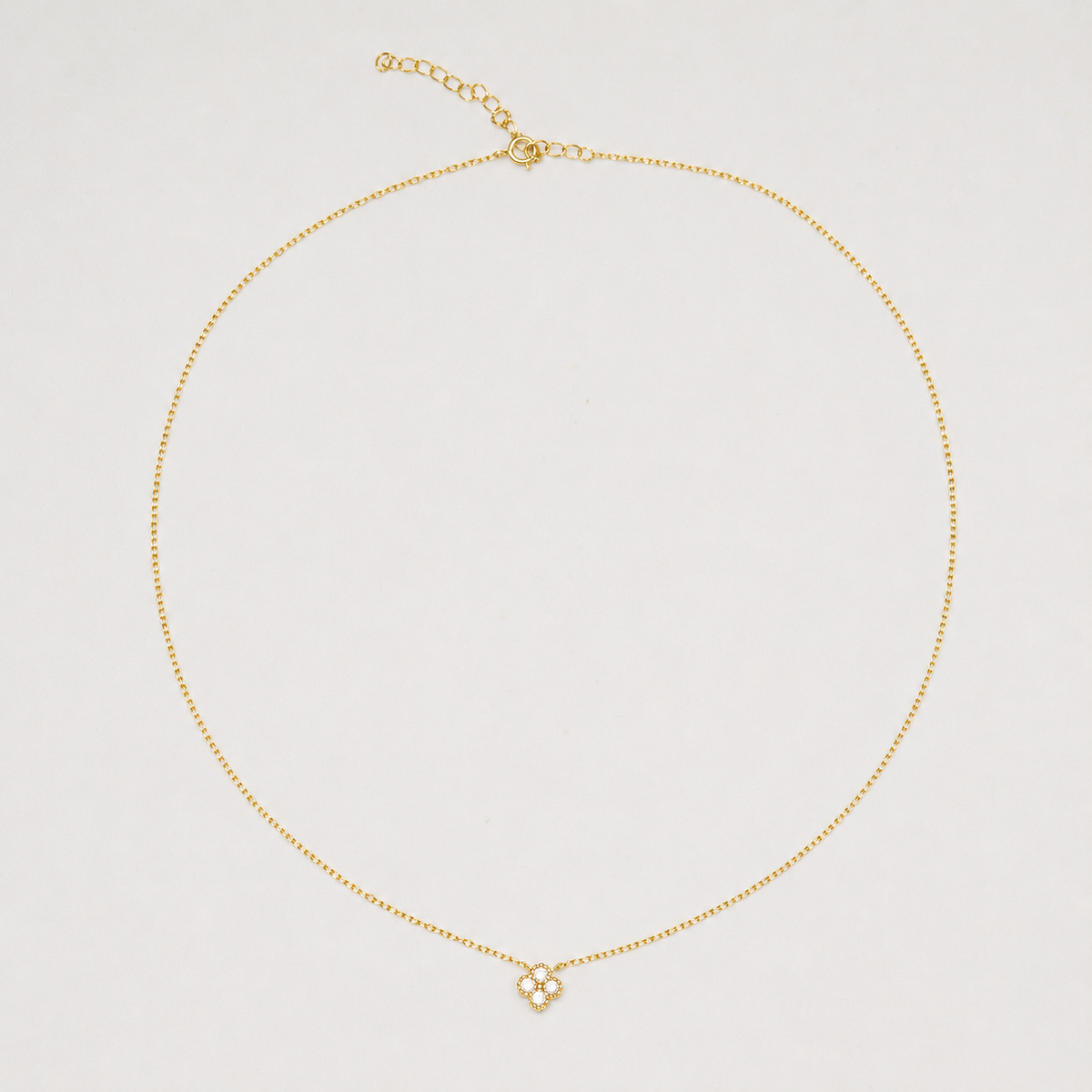 Gold-plated sterling silver necklace with a four-petal cubic zirconia pendant on a light background