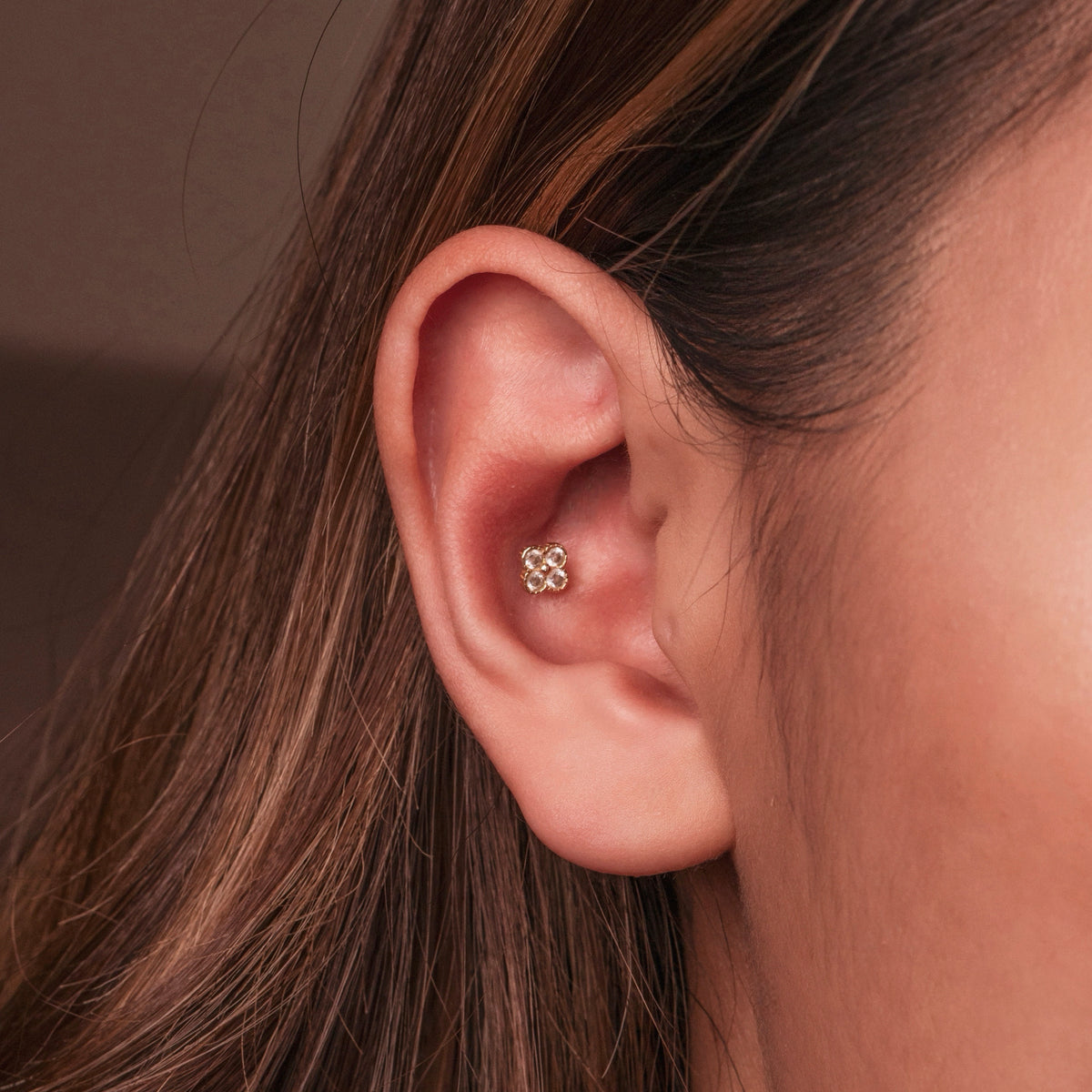 Gold-plated sterling silver round-back stud earring with a four-petal clear cubic zirconia design worn on the conch