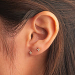 Gold-plated sterling silver stud earrings with four-petal clear cubic zirconia designs worn on the ear