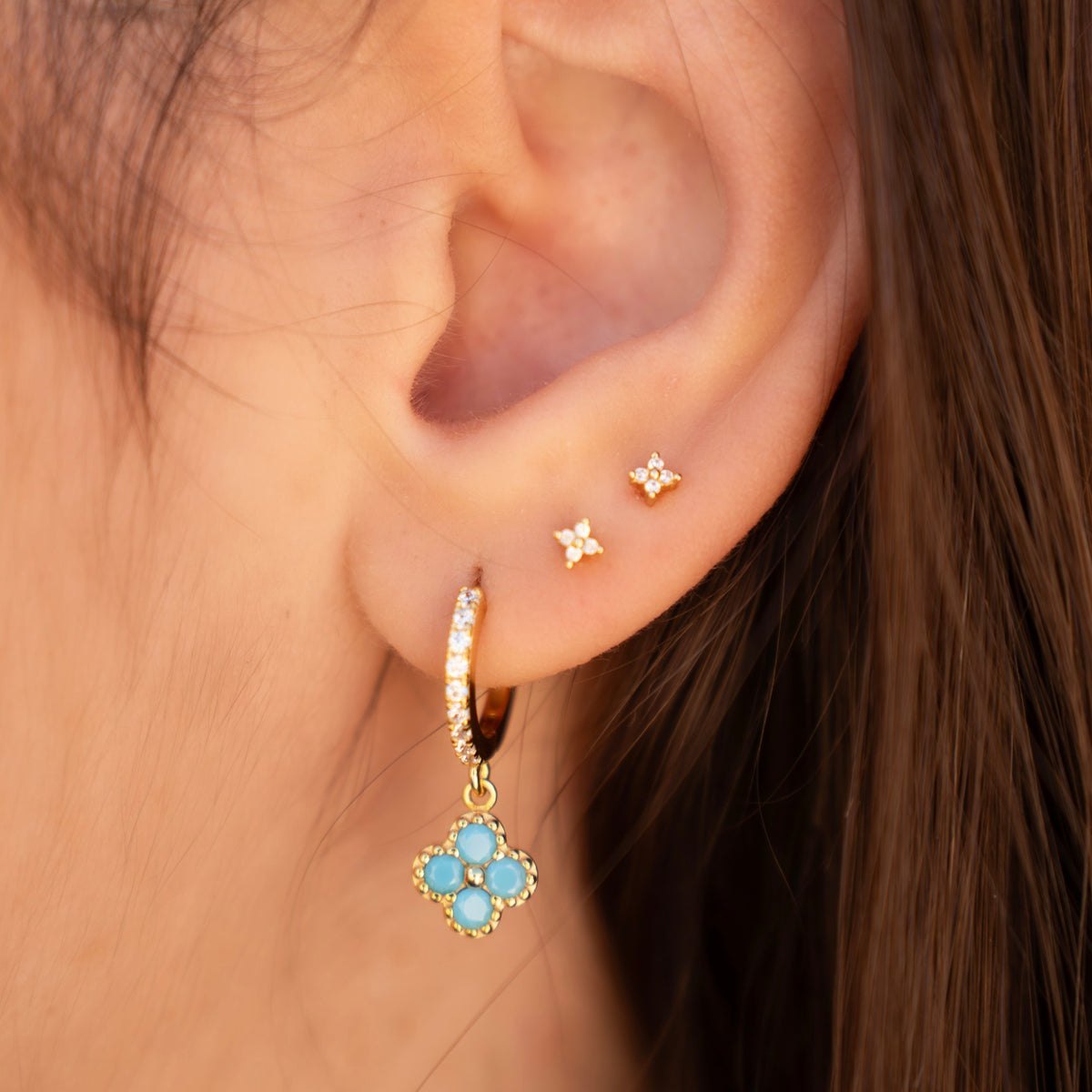 Gold-plated sterling silver stud earrings with four-petal clear cubic zirconia designs worn on the ear