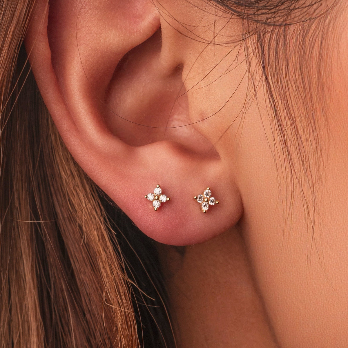 Gold-plated sterling silver stud earrings with four-petal clear cubic zirconia designs worn on the ear