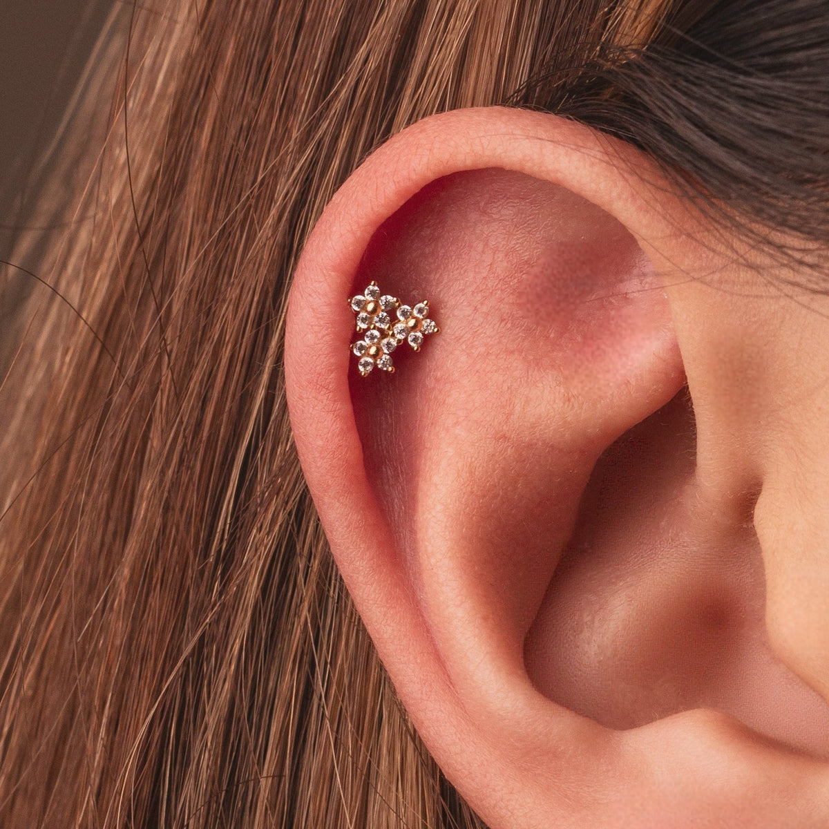 Gold-plated sterling silver huggie earring with a four-petal clear cubic zirconia flower design worn on the ear