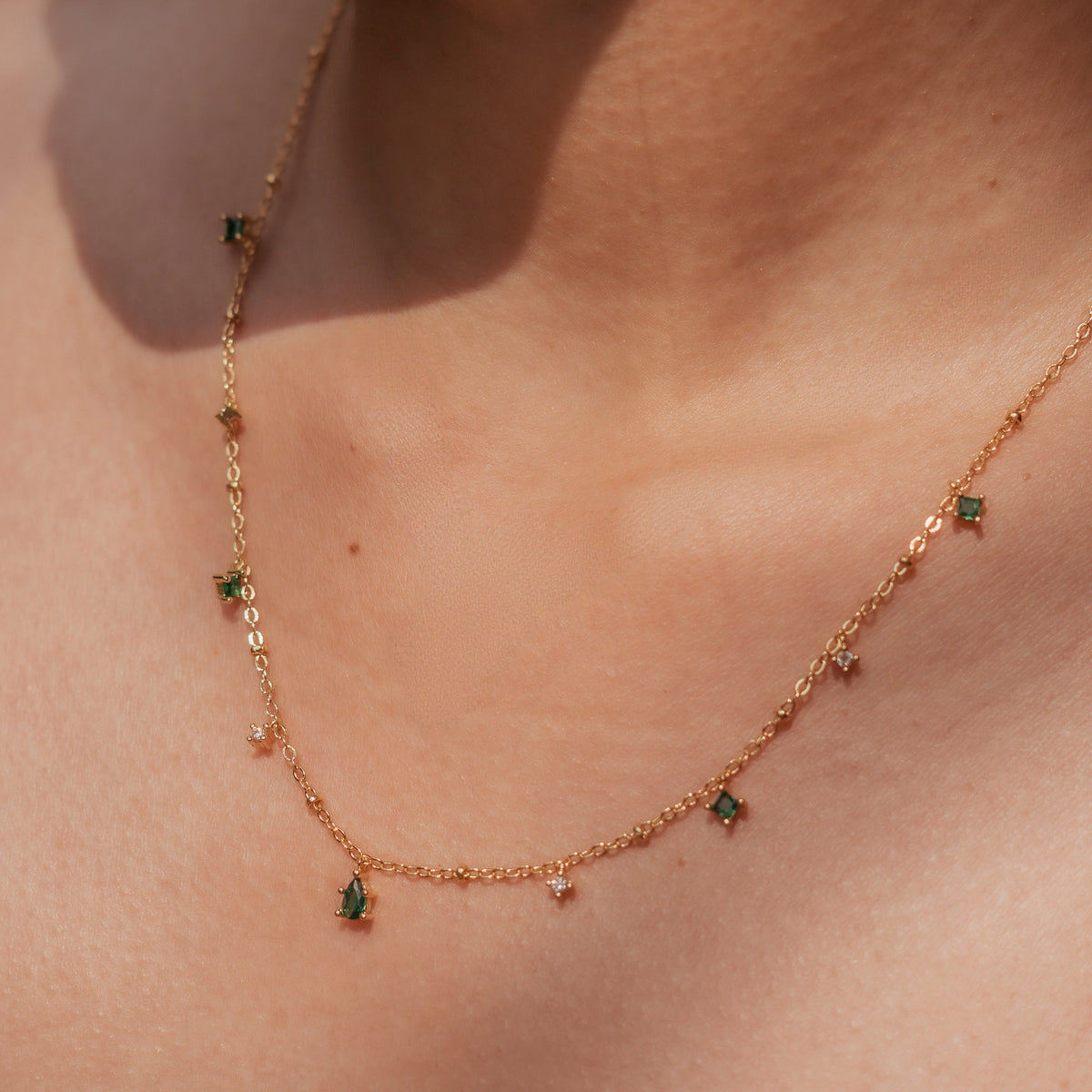 Gold-plated sterling silver necklace with small green cubic zirconia and clear stone charms worn around the neck