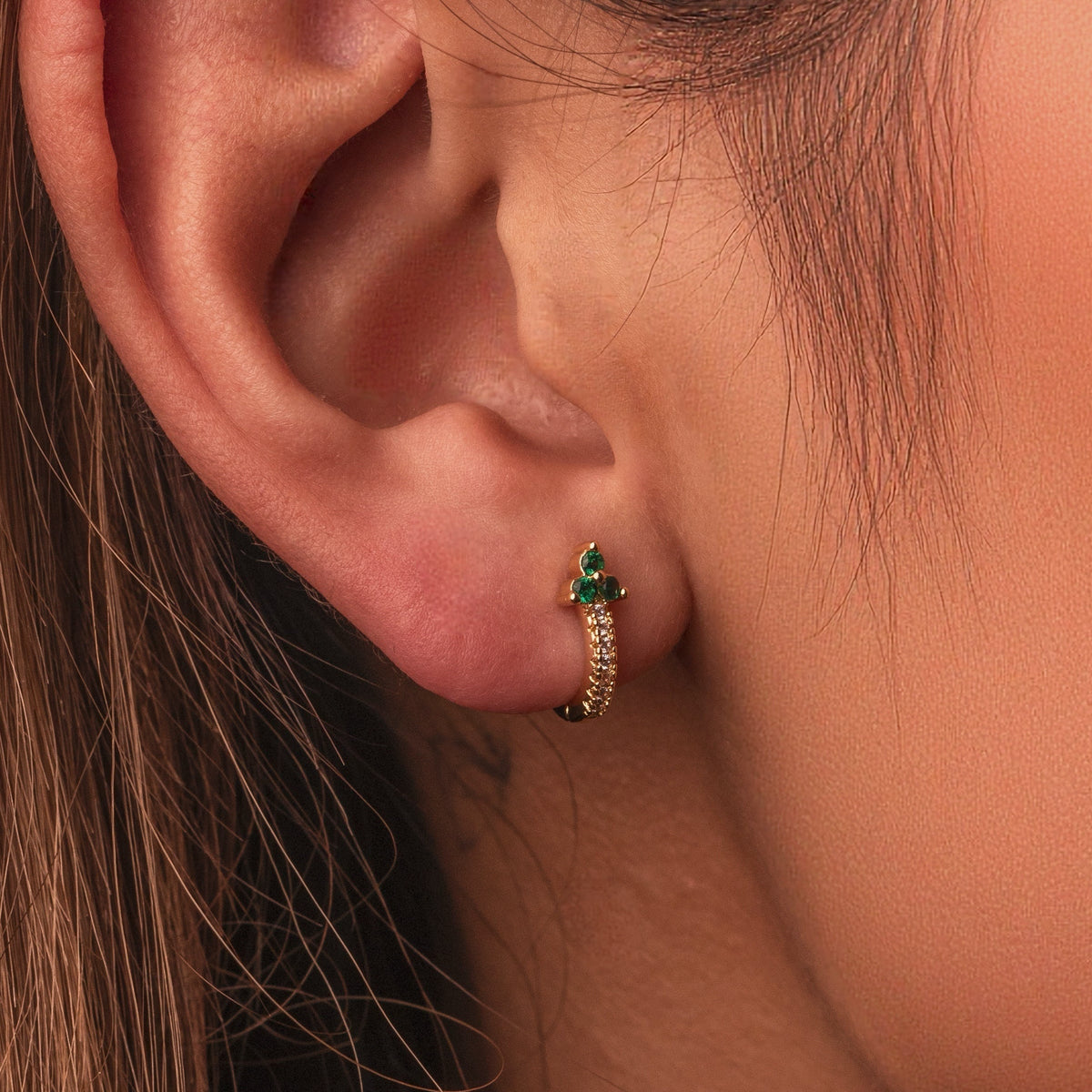 Gold-plated sterling silver huggie earrings with green and clear cubic zirconia stones worn on the ear