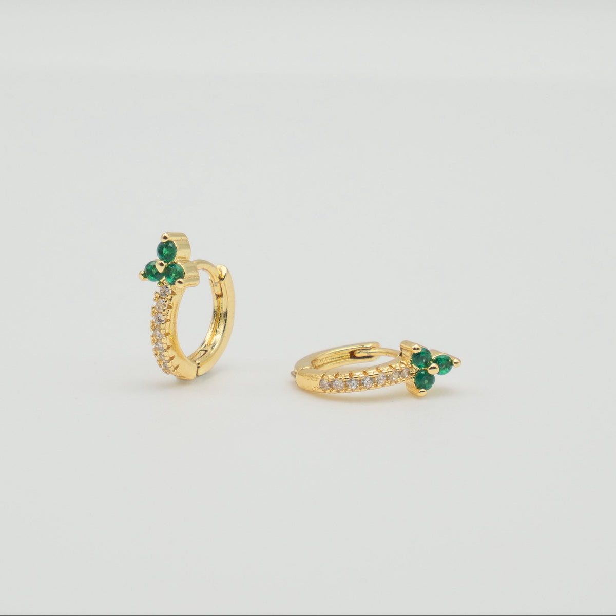 Gold-plated sterling silver huggie earrings with green and clear cubic zirconia stones on a light background