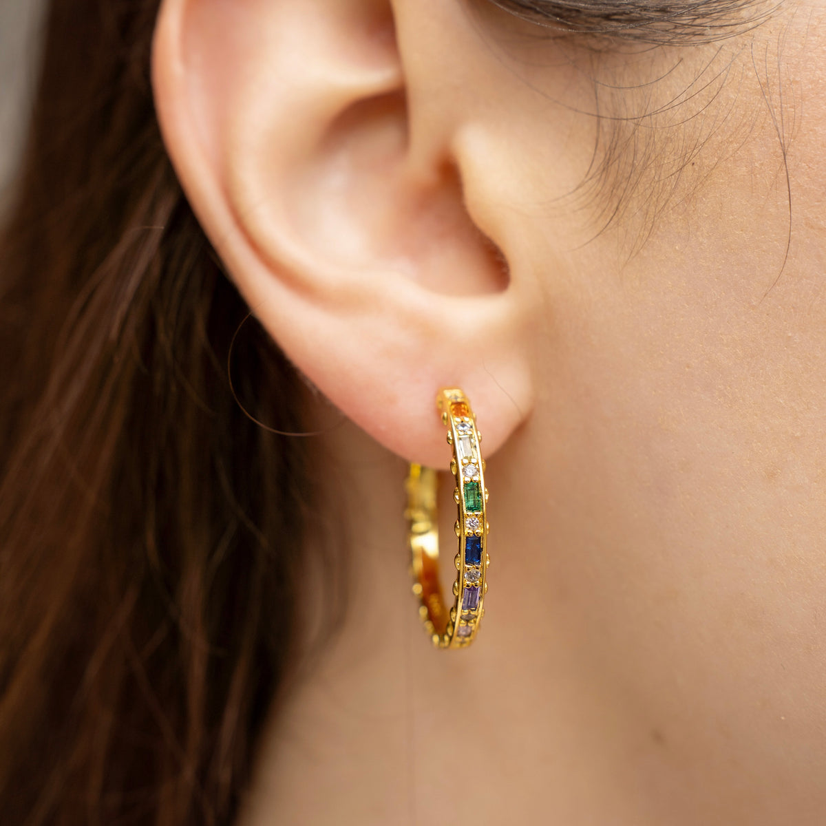 Gold-plated sterling silver hoop earrings with multicolor cubic zirconia stones worn on the ear