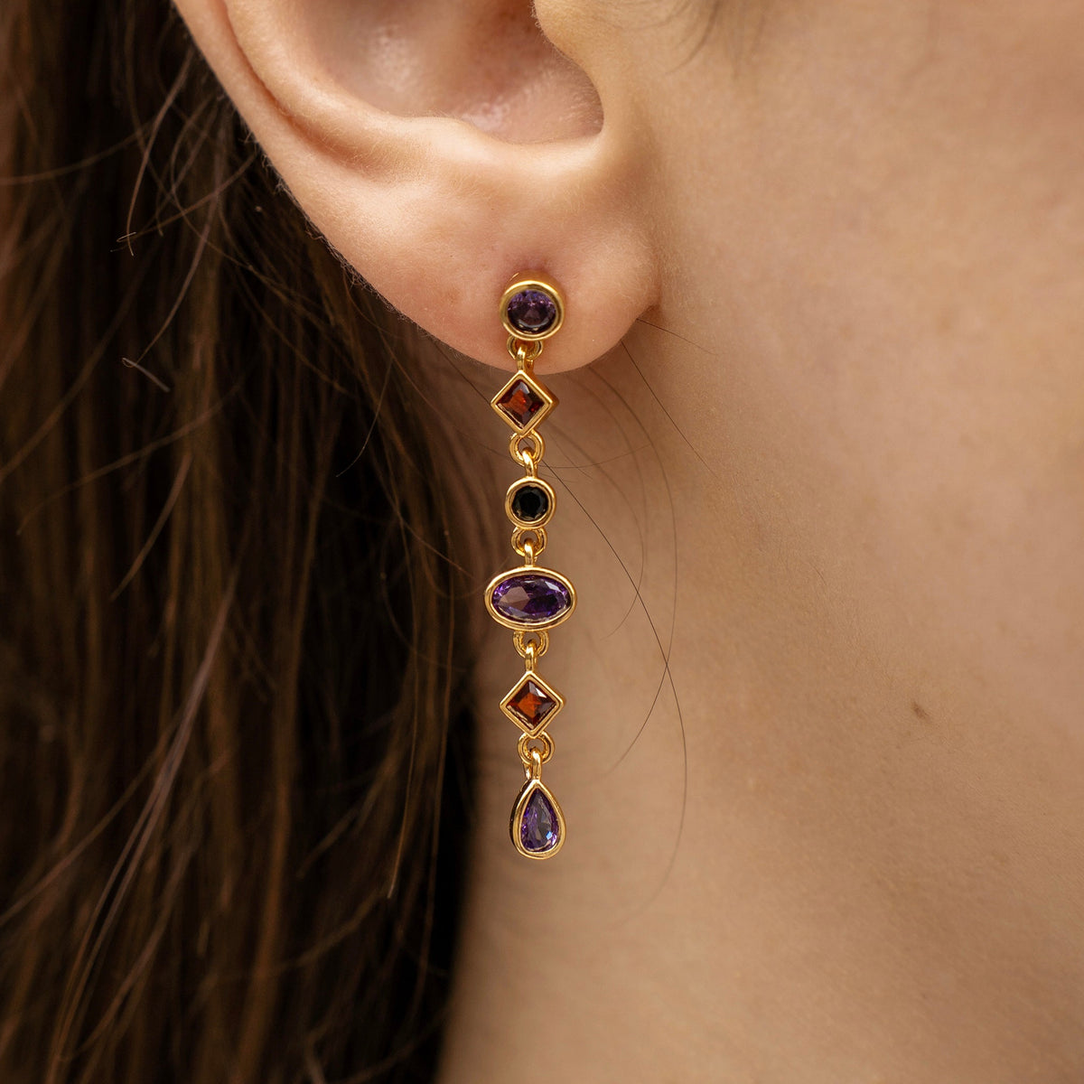 Gold-plated sterling silver drop earrings with purple, orange and black cubic zirconia stones worn on the ear