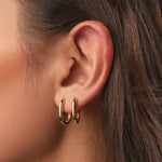 Gold-plated sterling silver oval hoop earrings with a smooth polished finish worn on ear