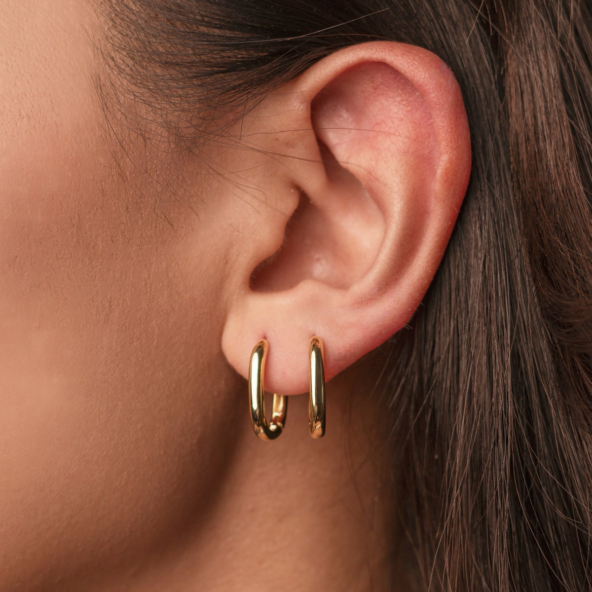 Gold-plated sterling silver oval hoop earrings with a smooth polished finish worn on ear