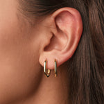 Gold-plated sterling silver oval hoop earrings with a smooth polished finish worn on ear