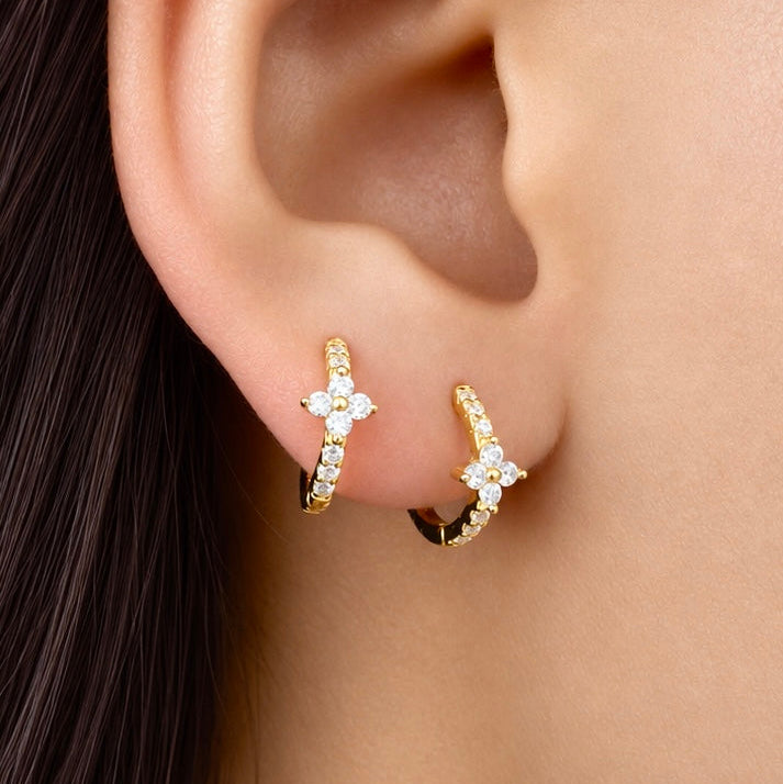 Gold-plated sterling silver huggie earrings with clear cubic zirconia pavé stones and a small clover detail worn on ear