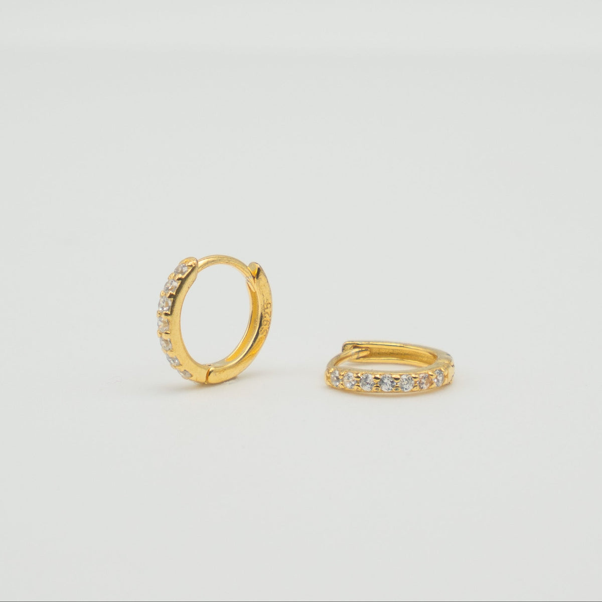Gold-plated sterling silver huggie earrings with clear cubic zirconia pavé stones on a light background