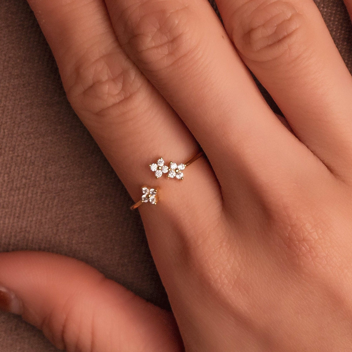 Gold-plated sterling silver ring with three flower motifs set with clear cubic zirconia stones, worn on the finger