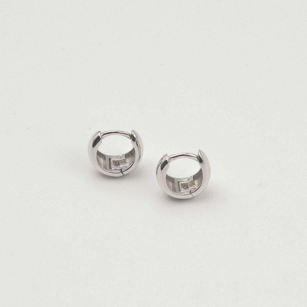 Rhodium-plated sterling silver chunky huggie earrings with a smooth polished finish on a light background