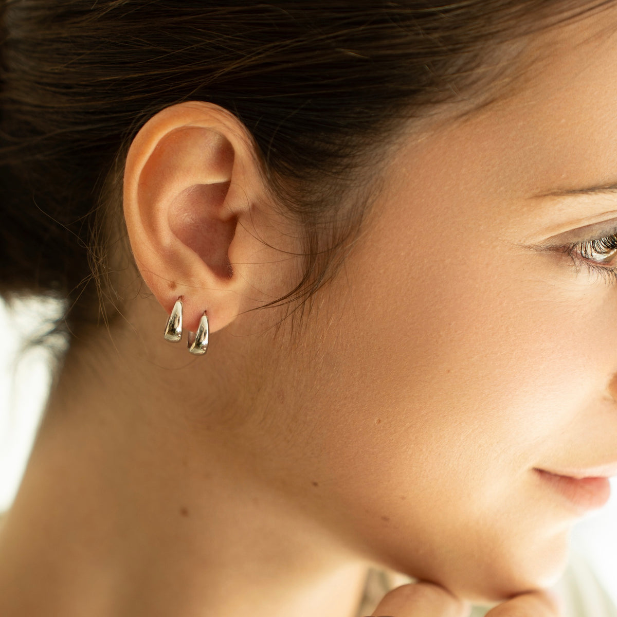 Rhodium-plated sterling silver chunky huggie earrings with a smooth polished finish worn on ear