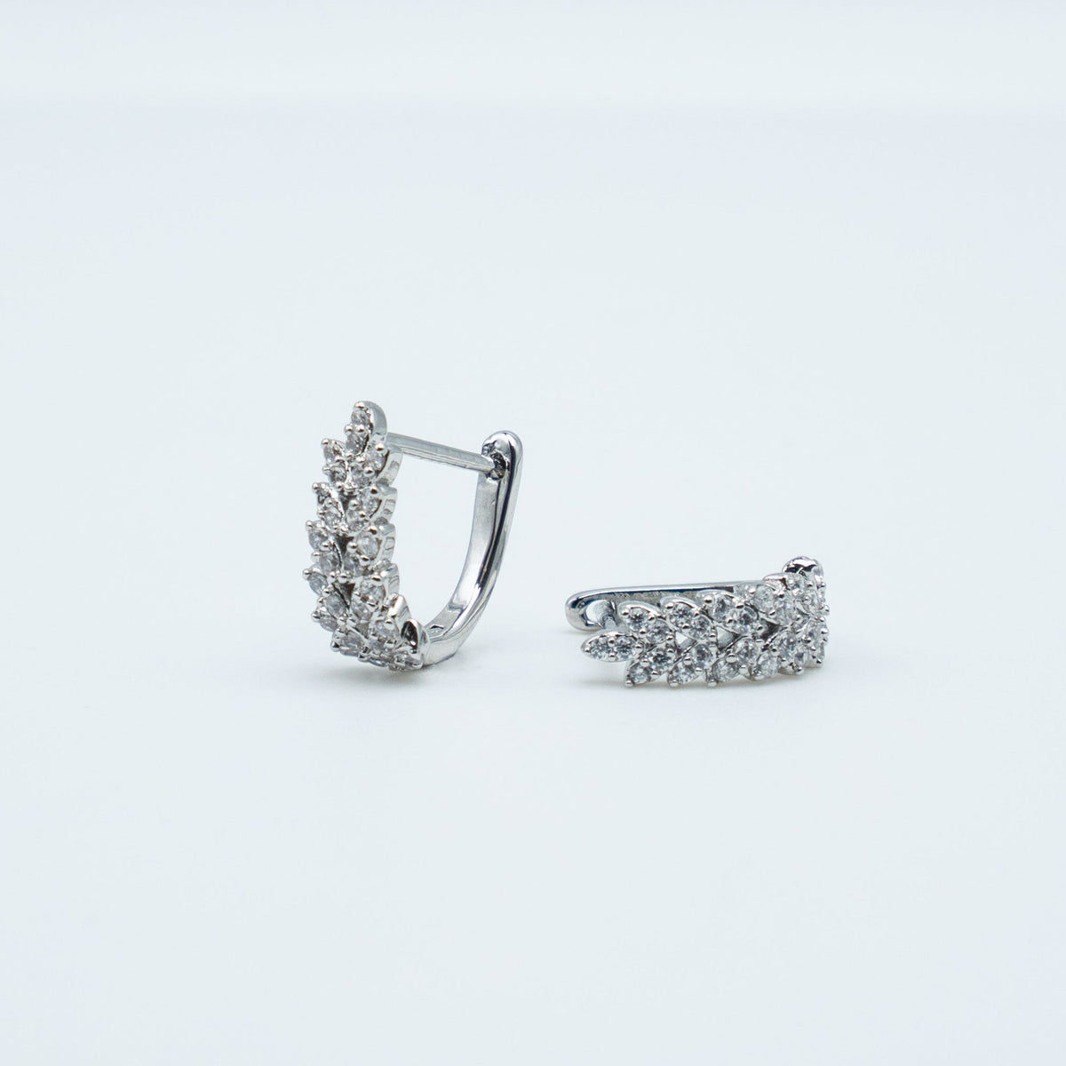 Rhodium-plated sterling silver huggie earrings with clustered clear cubic zirconia stones on a light background