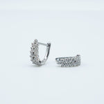 Rhodium-plated sterling silver huggie earrings with clustered clear cubic zirconia stones on a light background