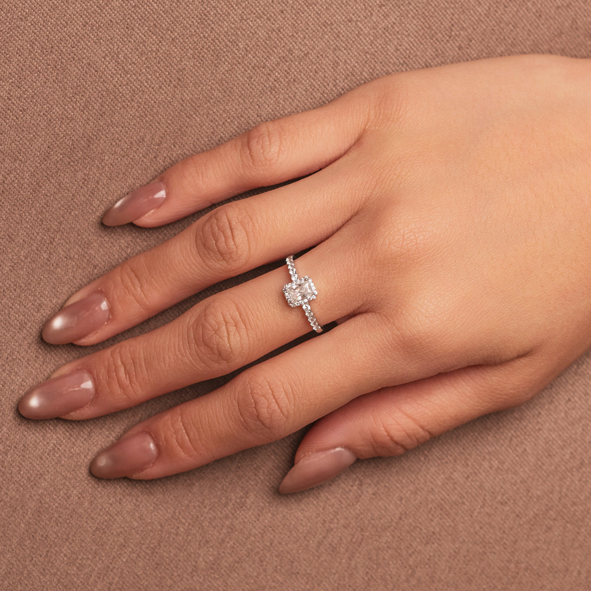 Rhodium-plated sterling silver solitaire ring with a cushion-cut moissanite center stone and pavé band worn on the finger