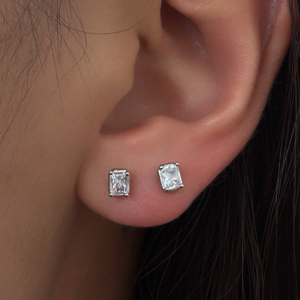 Rhodium-plated sterling silver stud earrings with emerald-cut clear cubic zirconia stones worn on ear