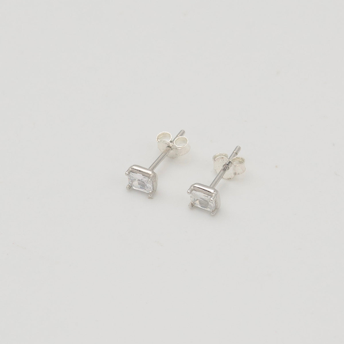 Rhodium-plated sterling silver stud earrings with emerald-cut clear cubic zirconia stones on a light background