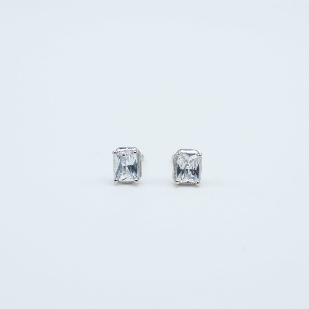 Rhodium-plated sterling silver stud earrings with emerald-cut clear cubic zirconia stones on a light background