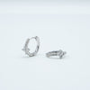 Rhodium-plated sterling silver huggie earrings with clear cubic zirconia floral details on a light background